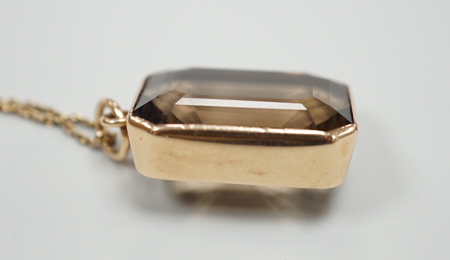 A yellow metal mounted smoky quartz pendant, 24mm, on a yellow metal fine link chain(a.f.), gross weight 15.6 grams.